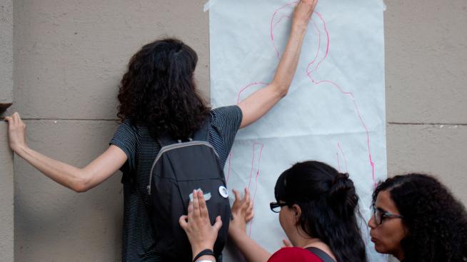 Una joven pega en la pared de la fachada de Filo una silueta dibujada en un papel afiche blanco.