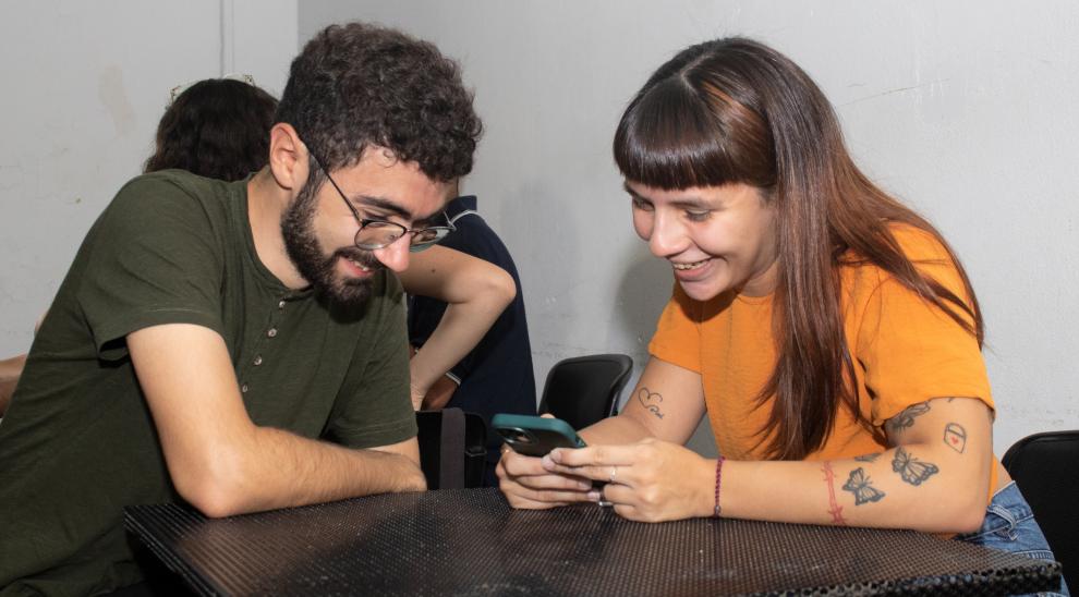 Dos estudiantes miran un celular y se ríen. 