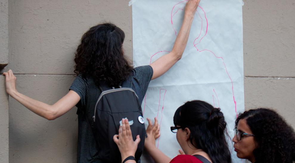 Una joven pega en la pared de la fachada de Filo una silueta dibujada en un papel afiche blanco. 