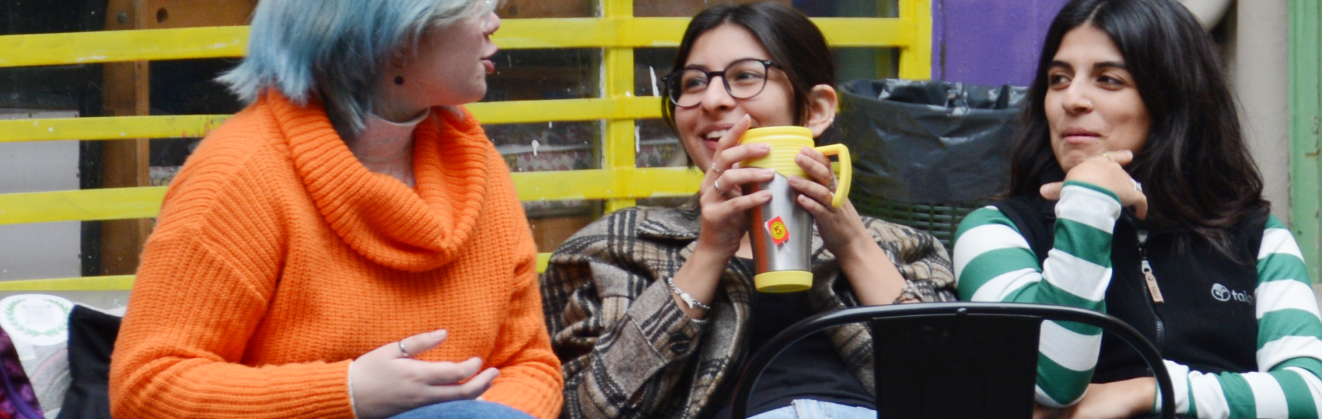 Tres jóvenes conversan sonrientes en un banco del patio de Puan. 